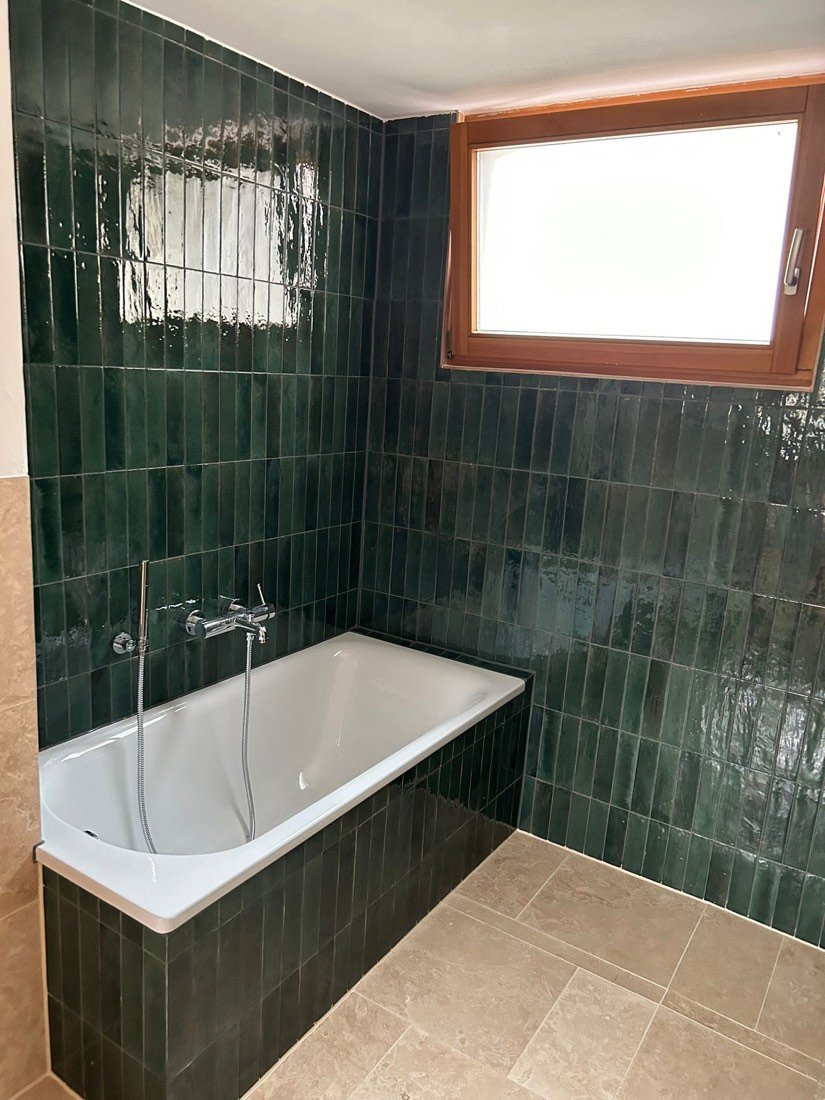 Badezimmer mit grünen Fliesen und weißer Badewanne